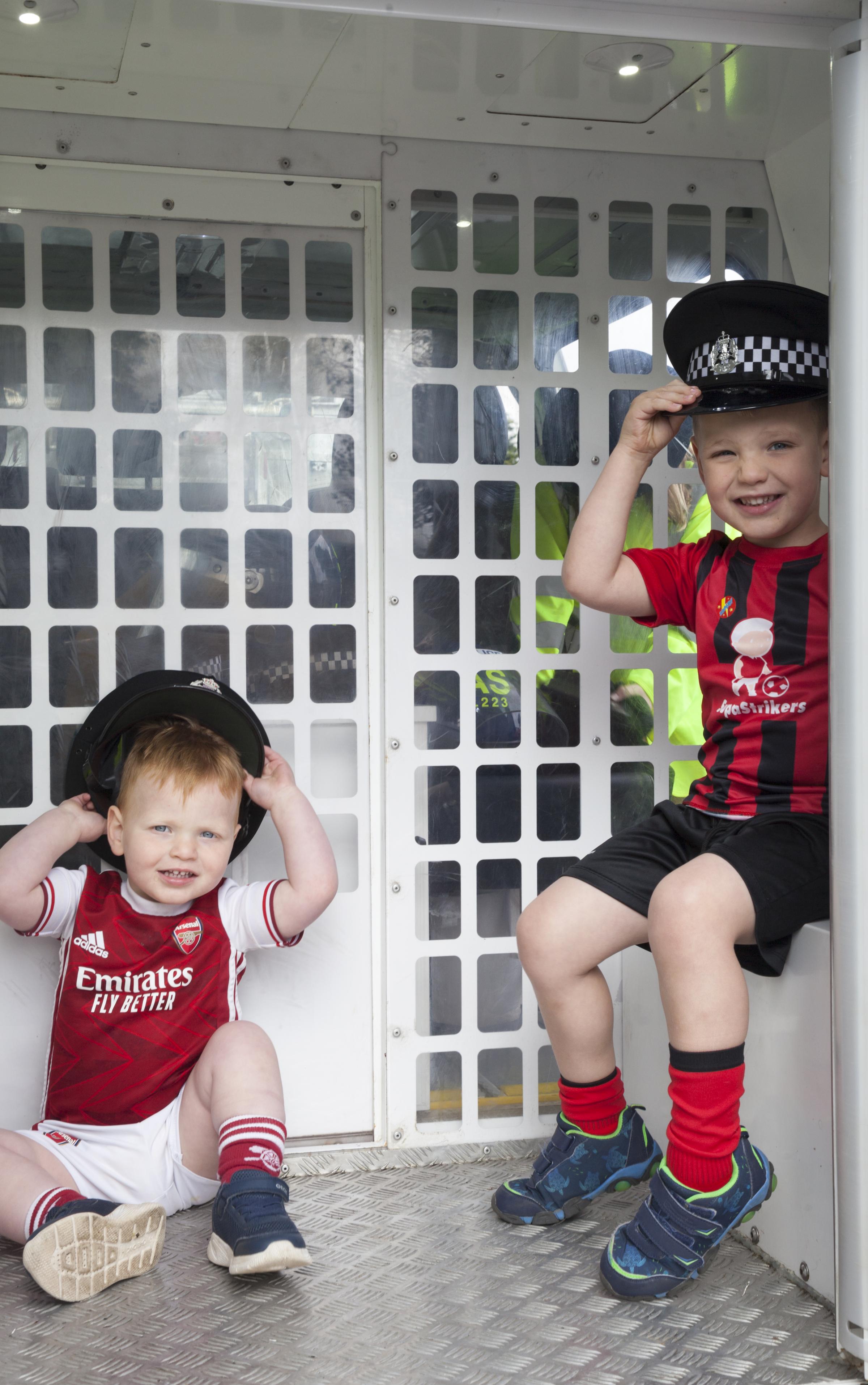 Fraser and Cameron Raeside in the back of a police van with police hats.