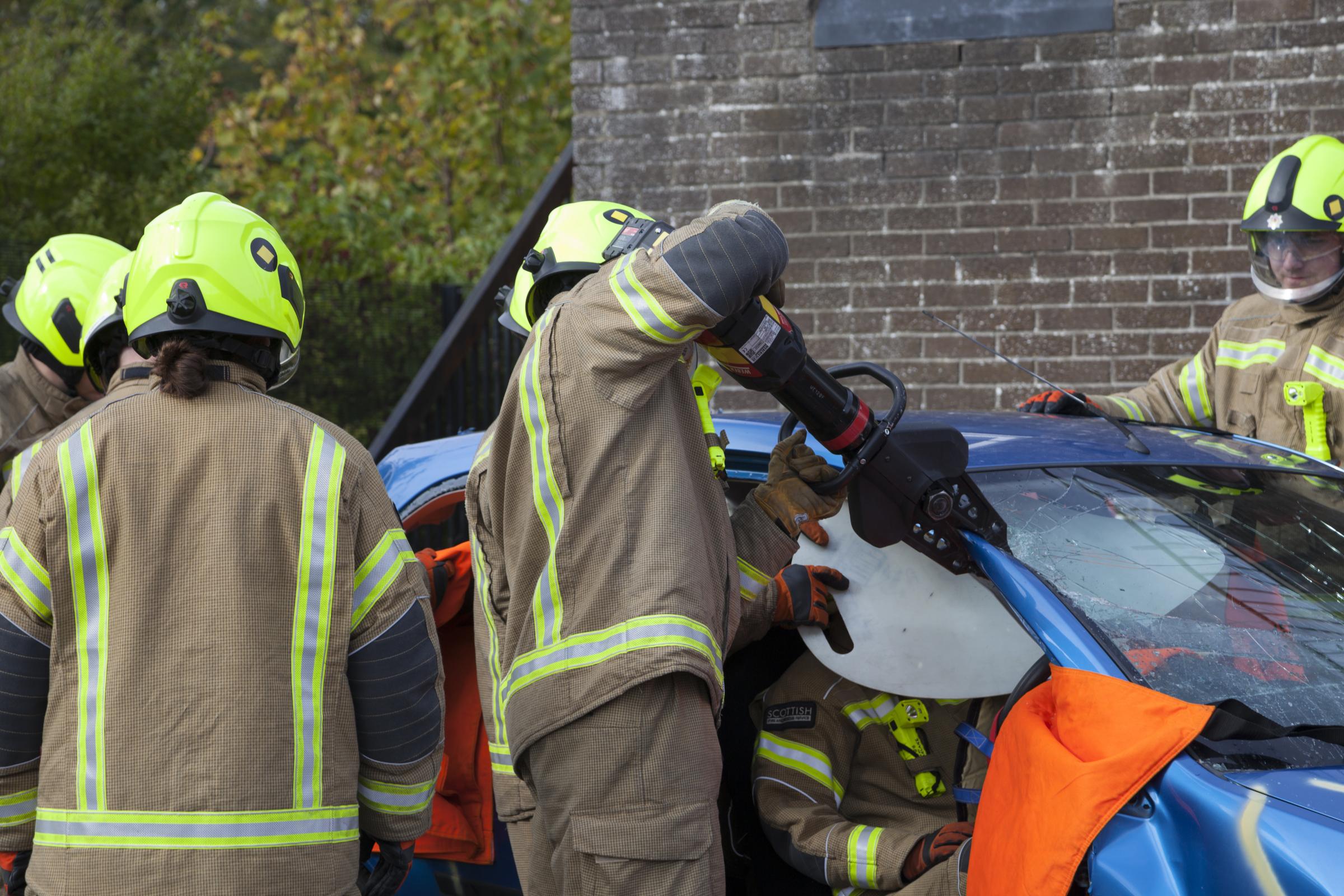 Fire fighters using heavy cuting equipment to remove a car roof to rescue driver.