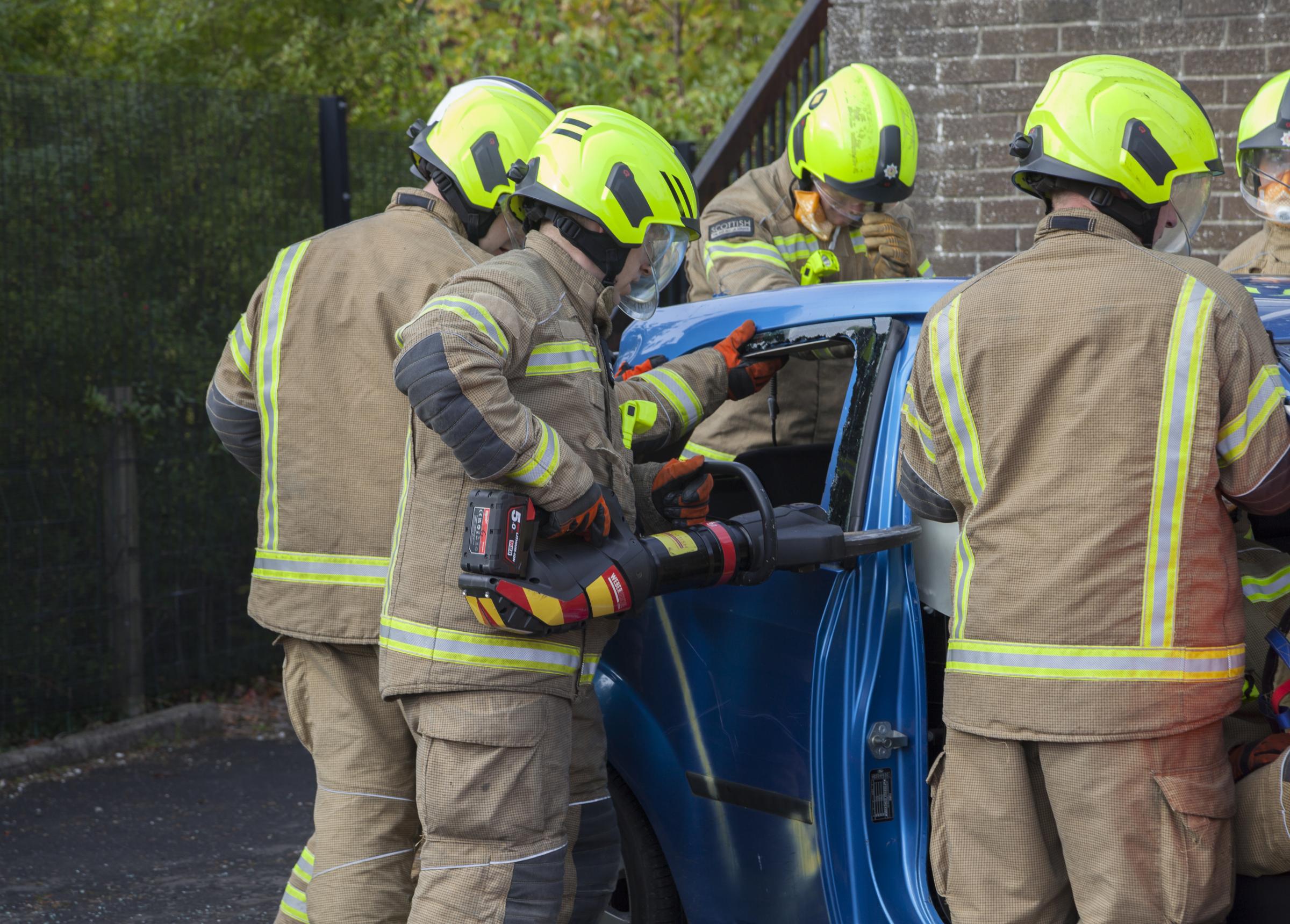 Fire fighters using heavy cutting equipment to remove a car roof to rescue driver.